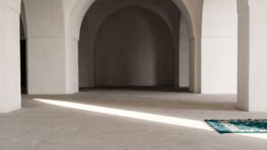 Sunlight falling across the floor of an empty arched prayer hall with a prayer mat laid out