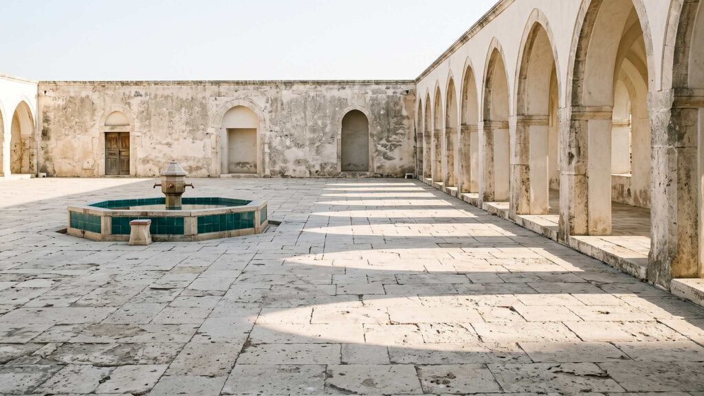 A stone courtyard with an arcade of arches and a low fountain in morning light