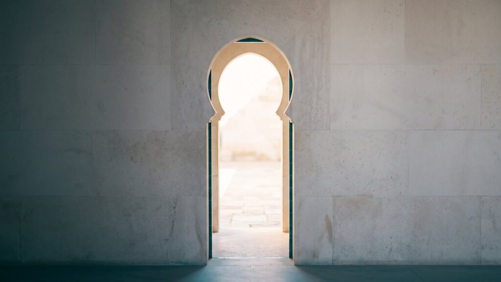 An arched doorway in a plaster wall opening onto bright daylight