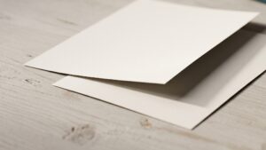 Two blank sheets of paper lying on a pale wooden table